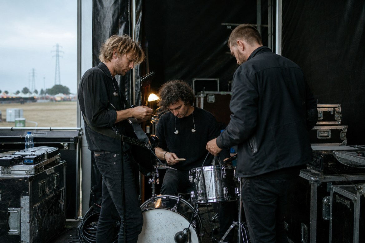 Musicians and a stage technician prepare instruments backstage at Aurora Fields.